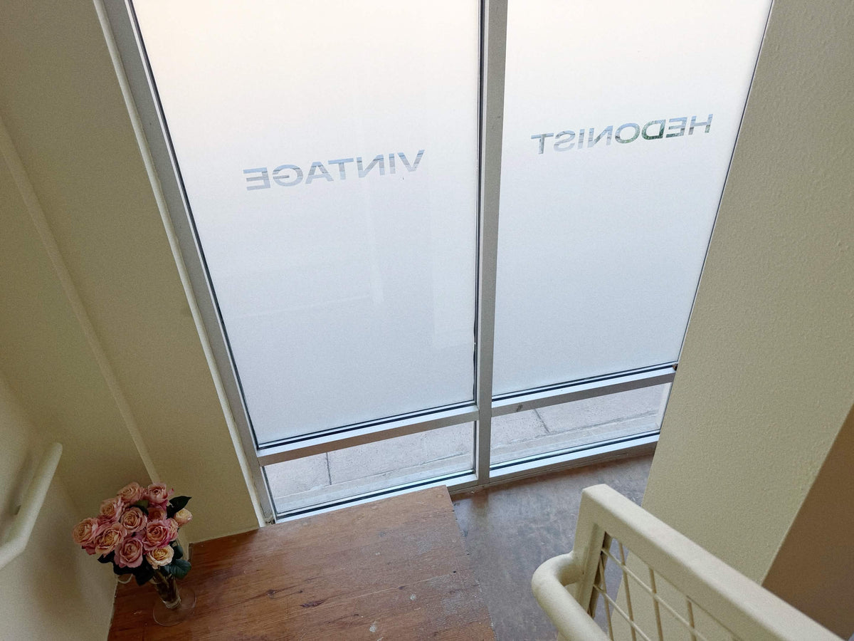Frosted glass sliding doors with mirrored branding text 'HEDONIST VINTAGE' and a flower vase with roses sitting on a wooden staircase landing.